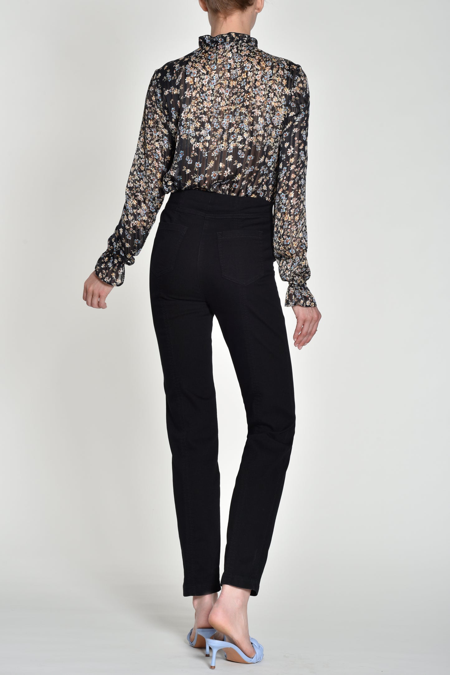 Person wearing a patterned blouse and black pants on a white background