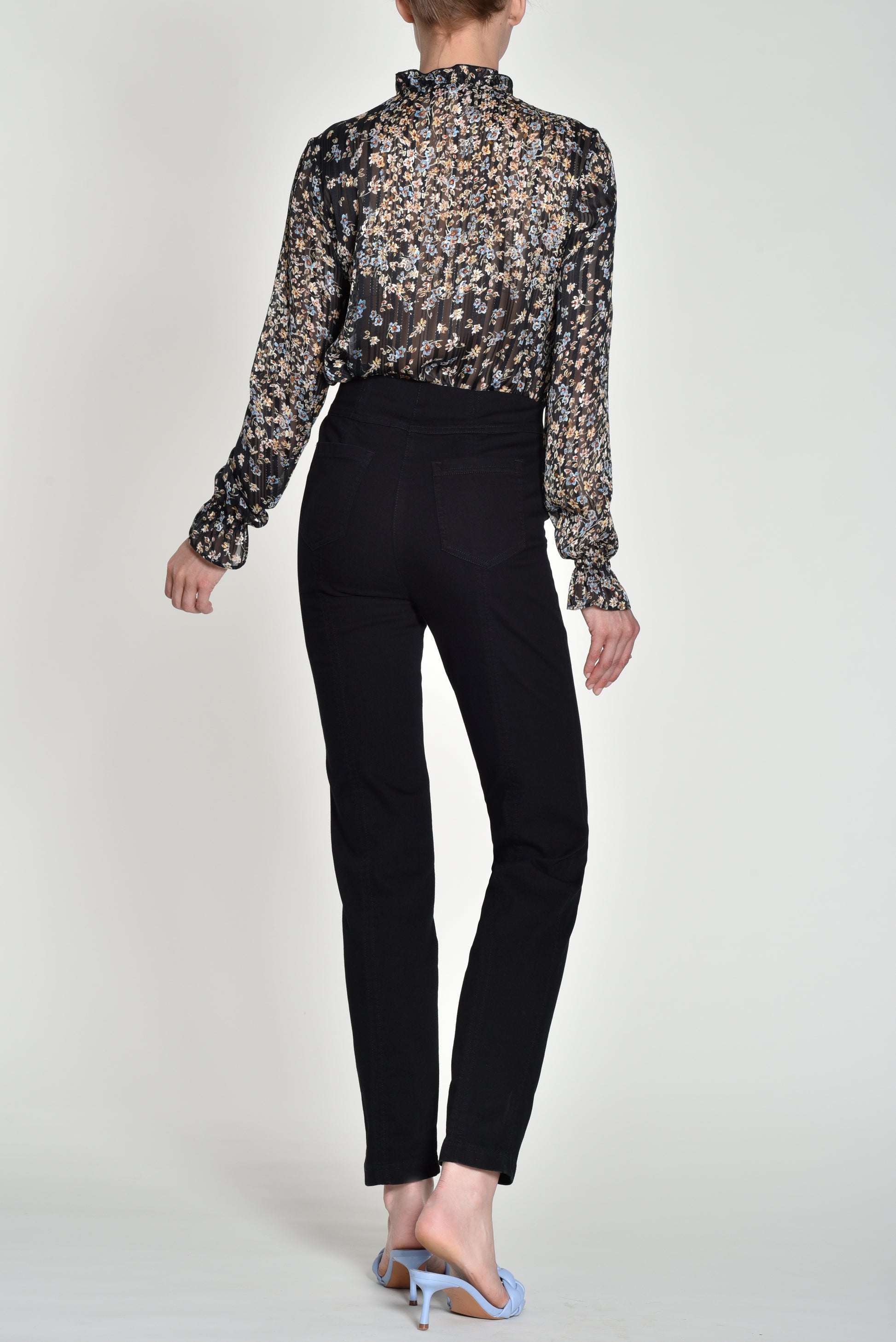 Person wearing a patterned blouse and black pants on a white background