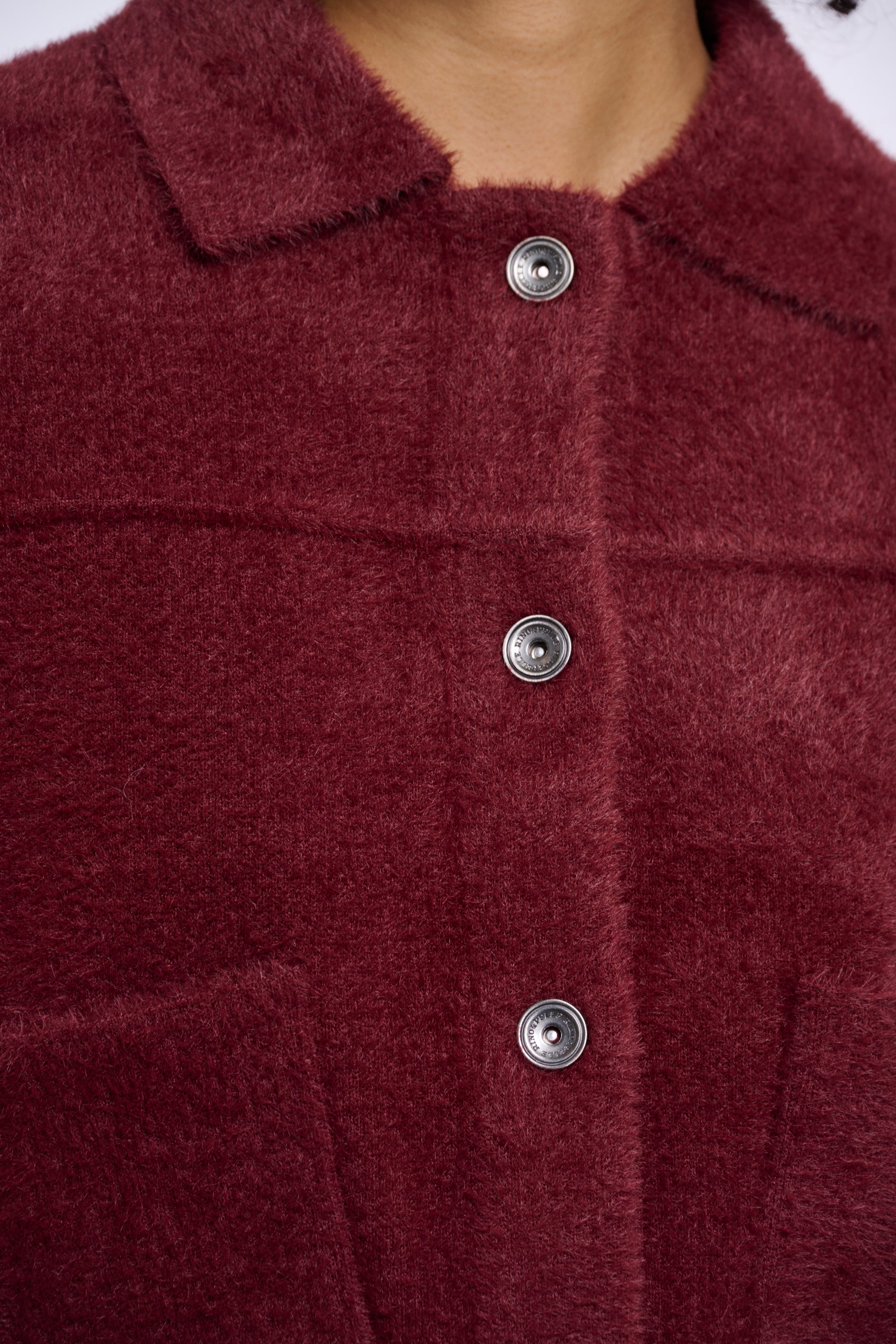 Close-up of a burgundy textured fabric with silver buttons