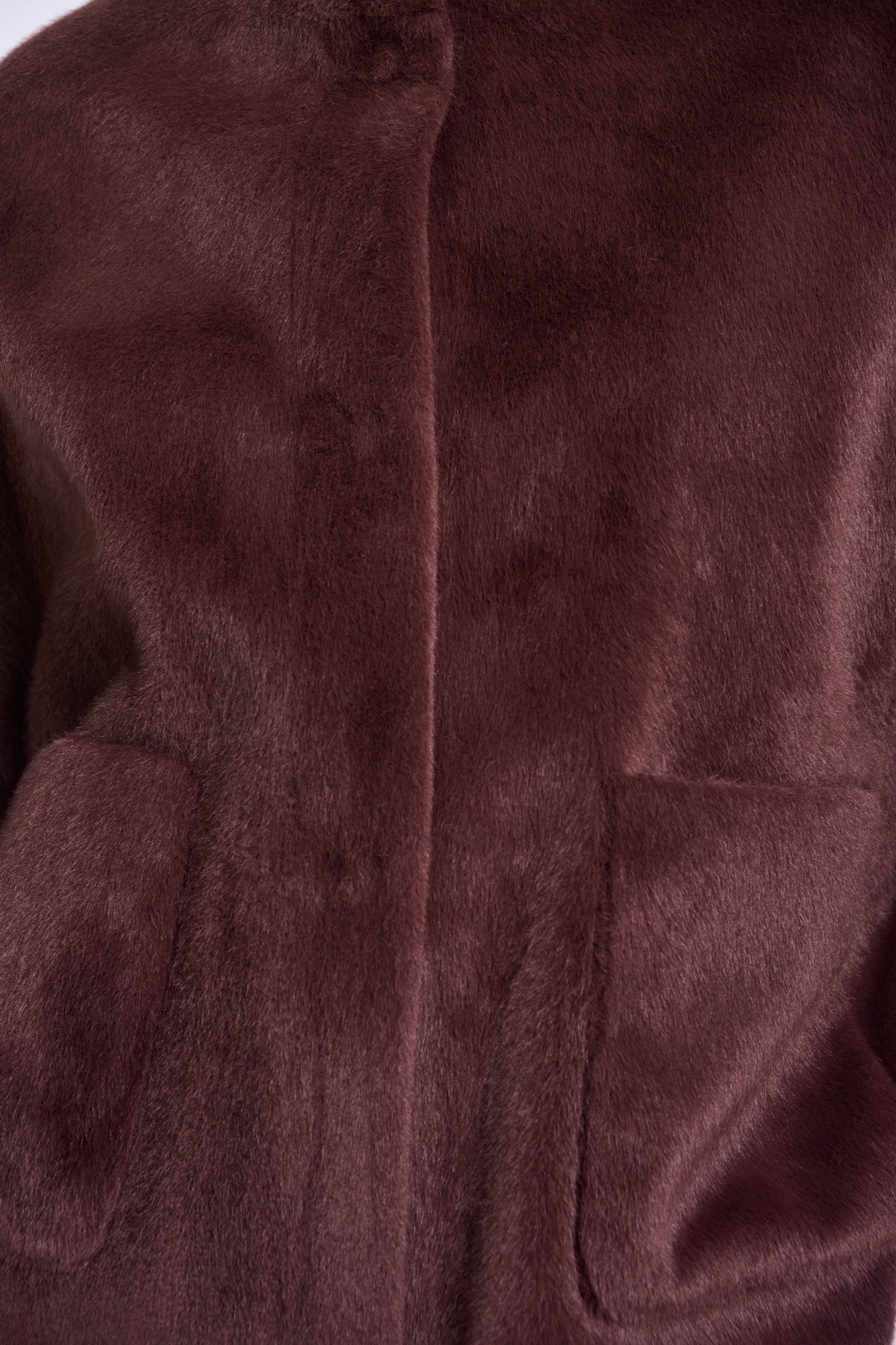 Close-up of a plush faux-fur or fleece garment in a deep plum-brown color, showing the soft texture and part of a front opening.