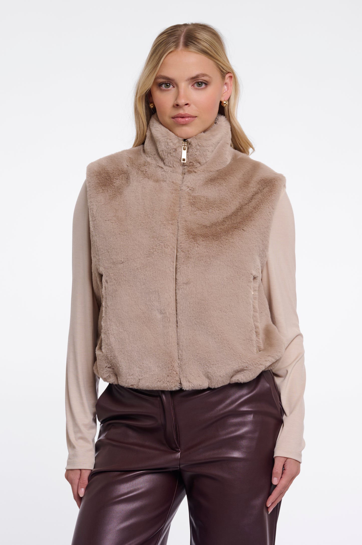 Woman wearing a beige fleece vest over a cream shirt with brown pants on a white background