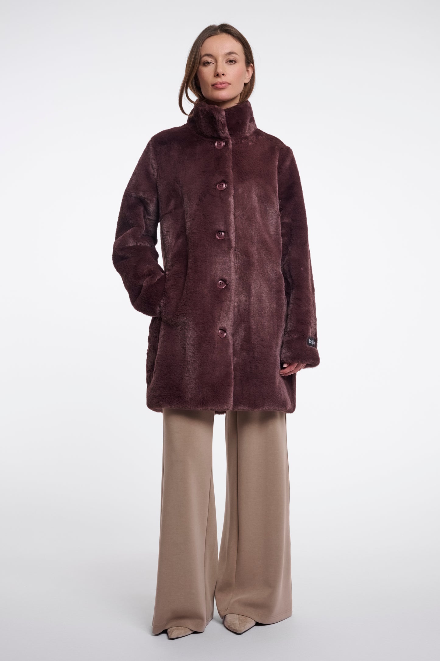 Woman wearing a brown coat and beige pants on a white background